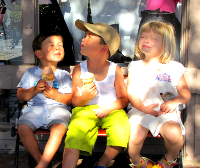 three littke kids eating ice cream cones with blissful look on their faced looking up eyes closed